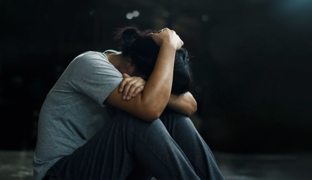 A person sitting on the floor with their head resting on their arms, appearing distressed, illustrating the emotional impact of PTSD.